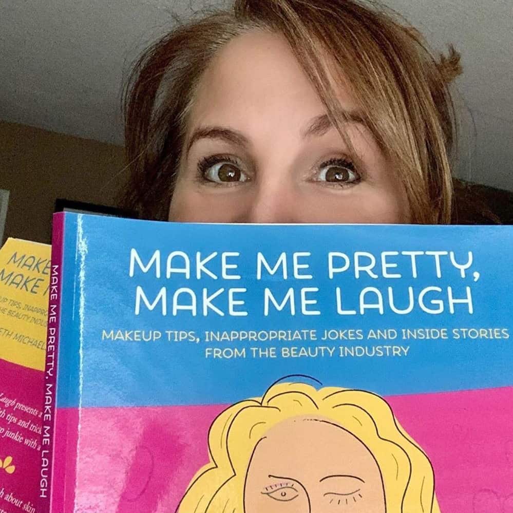 woman holding up a copy of Make Me Pretty, Make Me Laugh