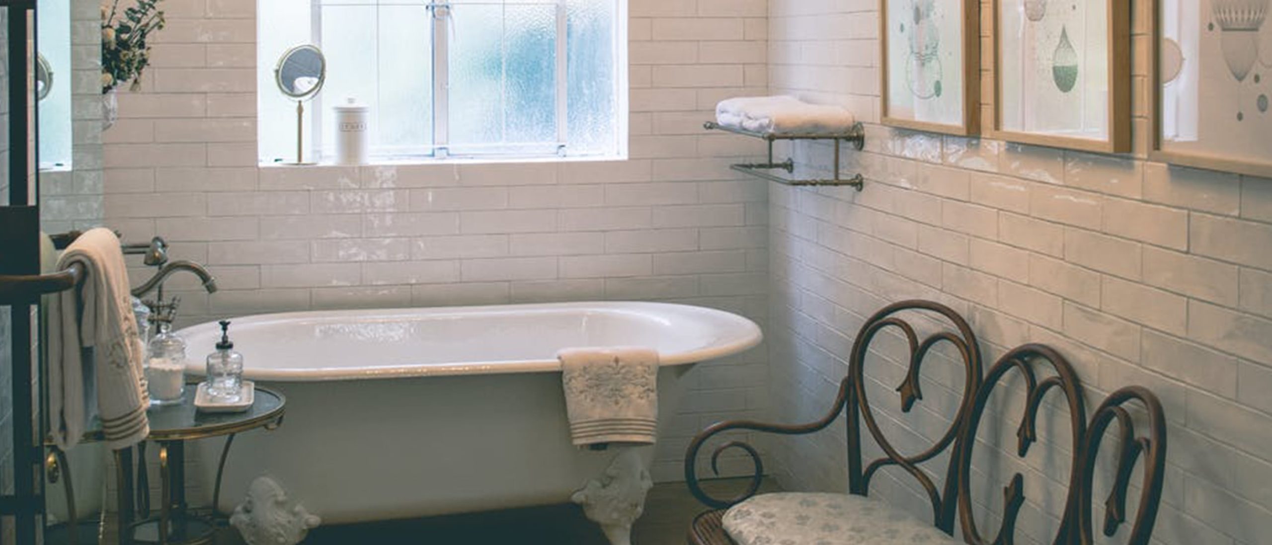clawfoot bathtub in white tile room with vintage seats and tile